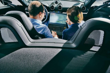 Blick über vom Rücksitz eines Autos auf eine Frau und einen Kunden, die das Boardsystem bedienen.