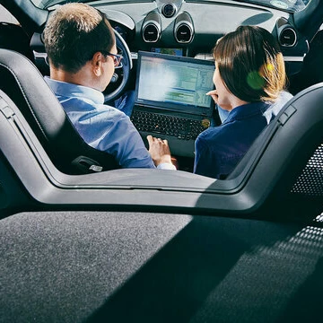 Blick über vom Rücksitz eines Autos auf eine Frau und einen Kunden, die das Boardsystem bedienen.